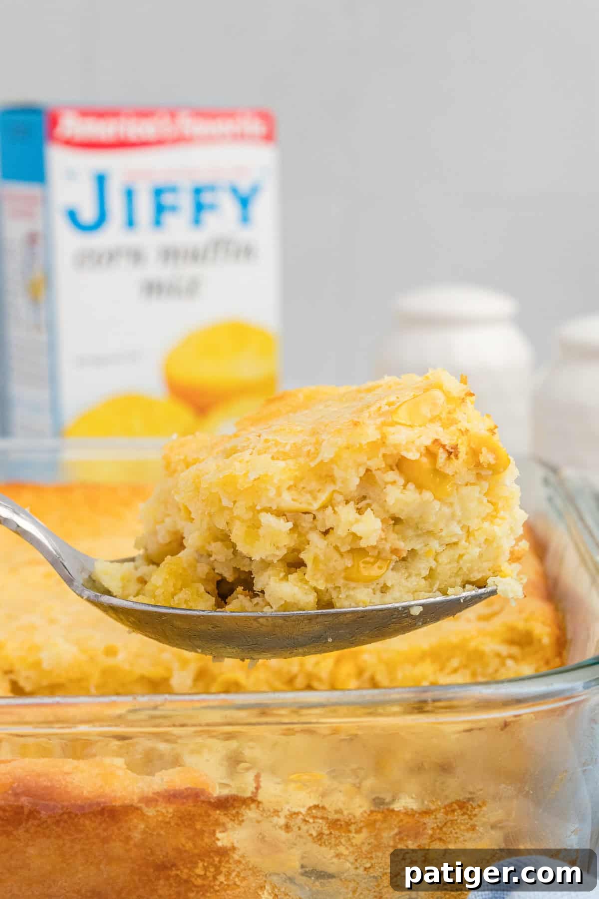 Golden Jiffy Cornbread and Creamed Corn Bake 8 A serving spoon scoops a large portion of Jiffy cornbread casserole with creamed corn and kernels visible, showing its moist and tender texture.