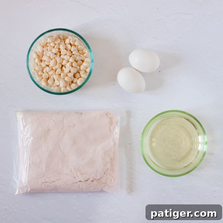 The four essential ingredients for strawberry cake mix cookies: white chocolate chips, vegetable oil, two eggs, and a box of strawberry cake mix.