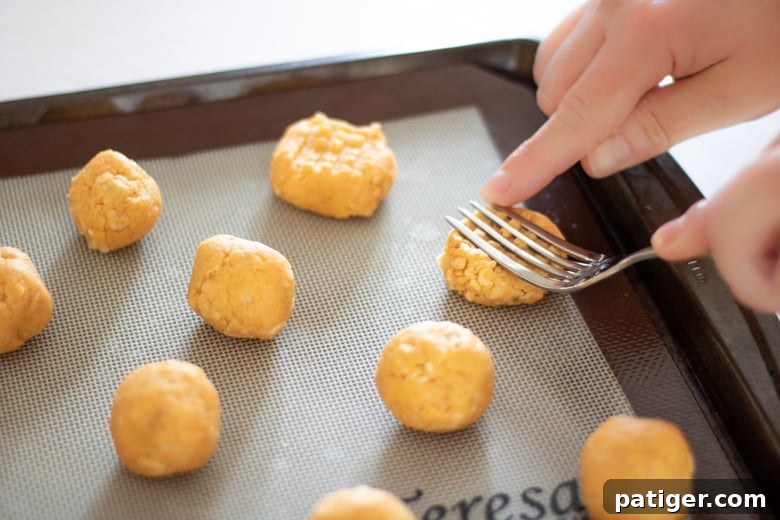 A fork pressing a criss-cross pattern onto a dough ball for cheese cookies