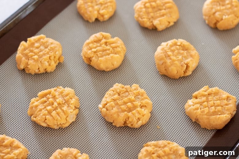 Cheese cookies with decorative fork lines arranged on a parchment-lined baking sheet, ready for baking