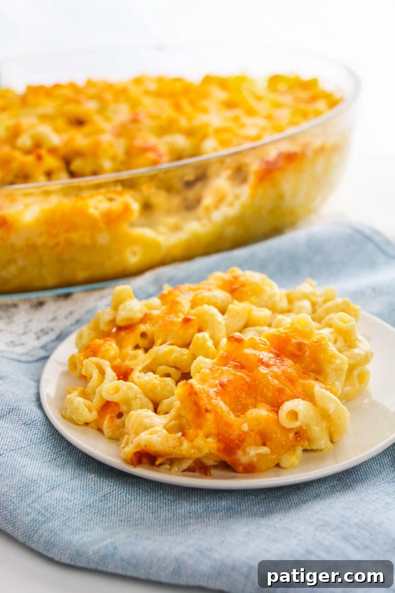 Elbow pasta with golden, creamy cheese sauce on a plate, with a full casserole dish of baked mac and cheese blurred in the background
