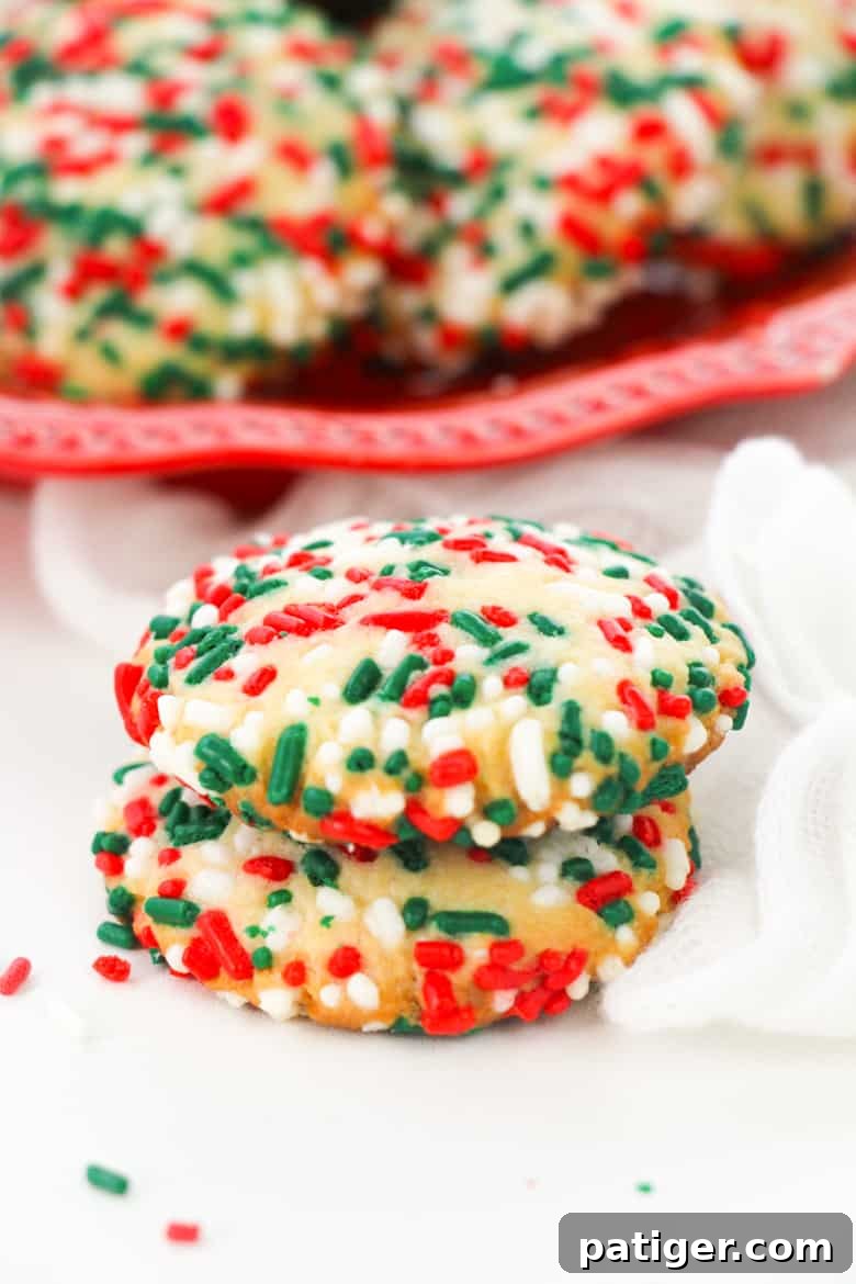 Baked Christmas sprinkle sugar cookies piled on a white plate, showcasing their festive colors and soft texture.