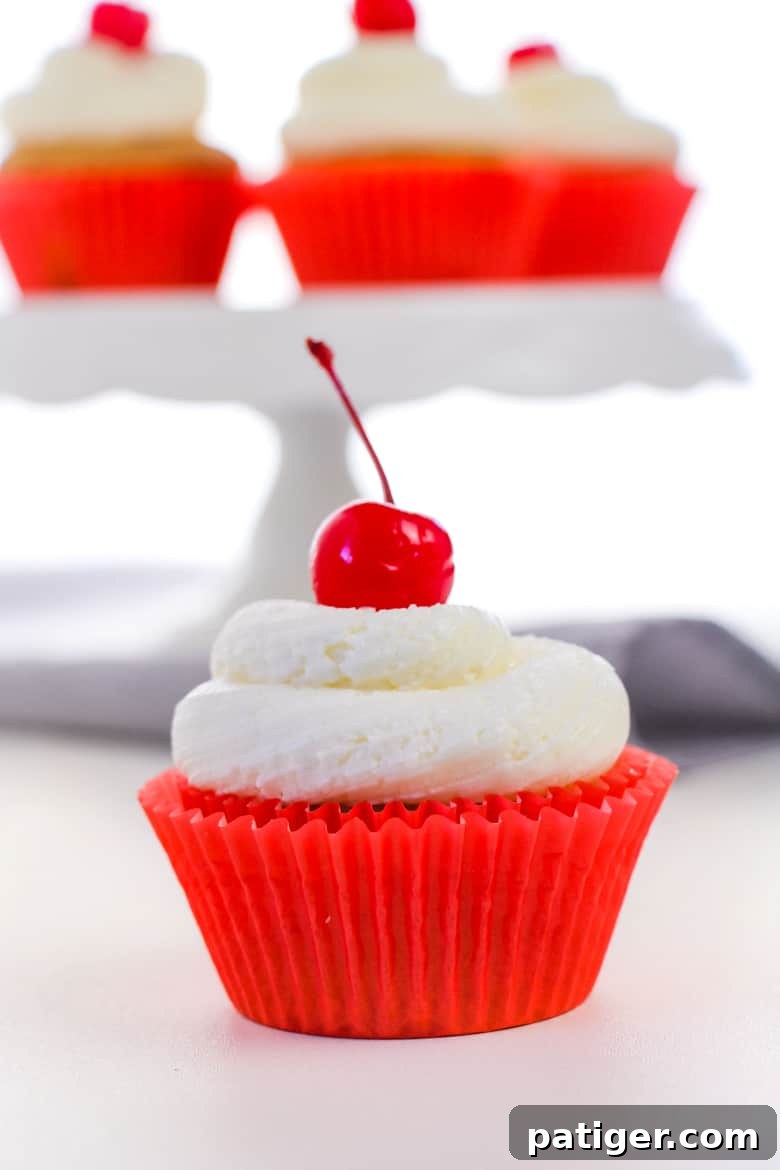Cupcakes in red liners topped with fluffy white icing and cherries