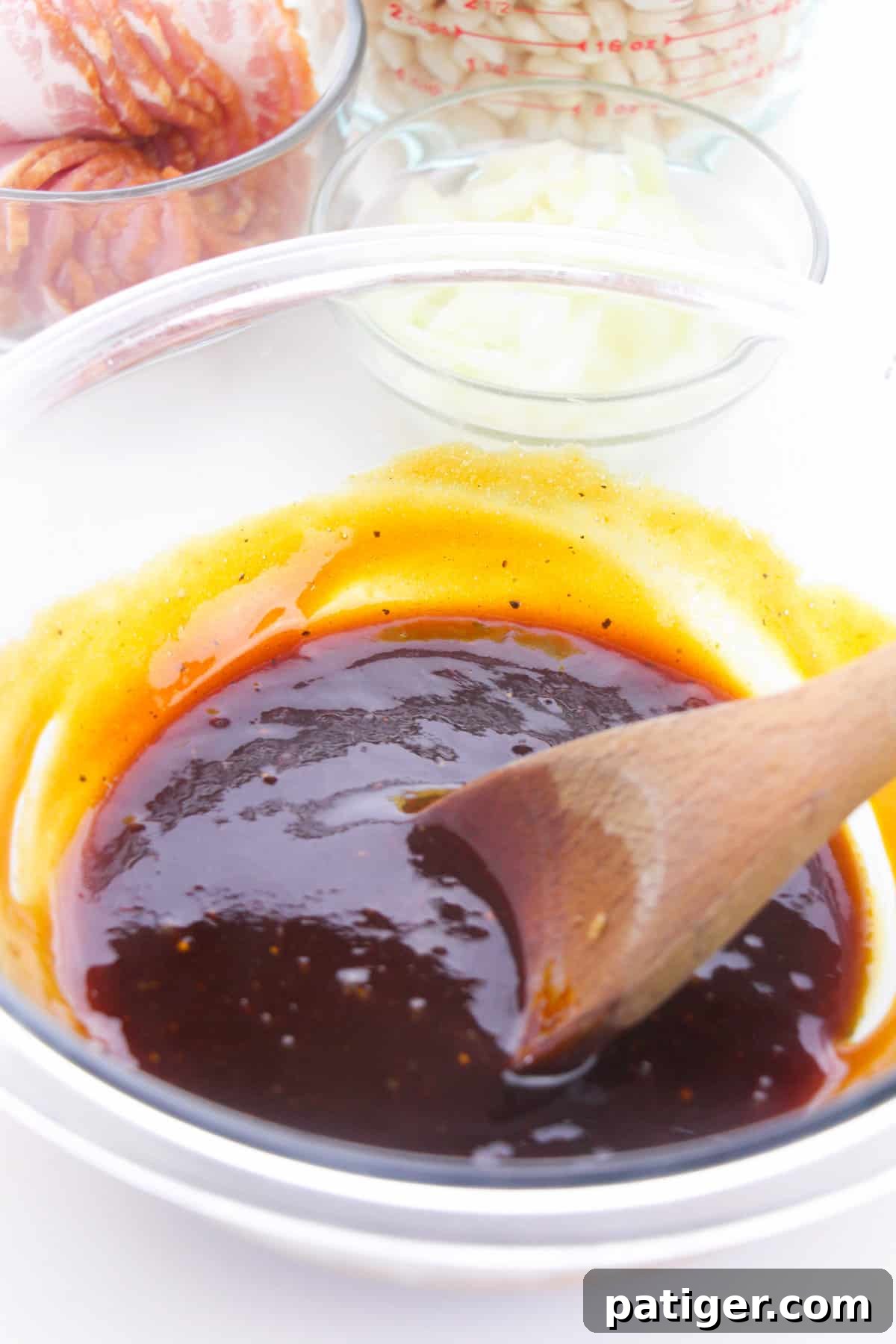 Ultimate Boston Baked Beans 6 Thick, dark brown sauce in a glass bowl with a wooden spoon.