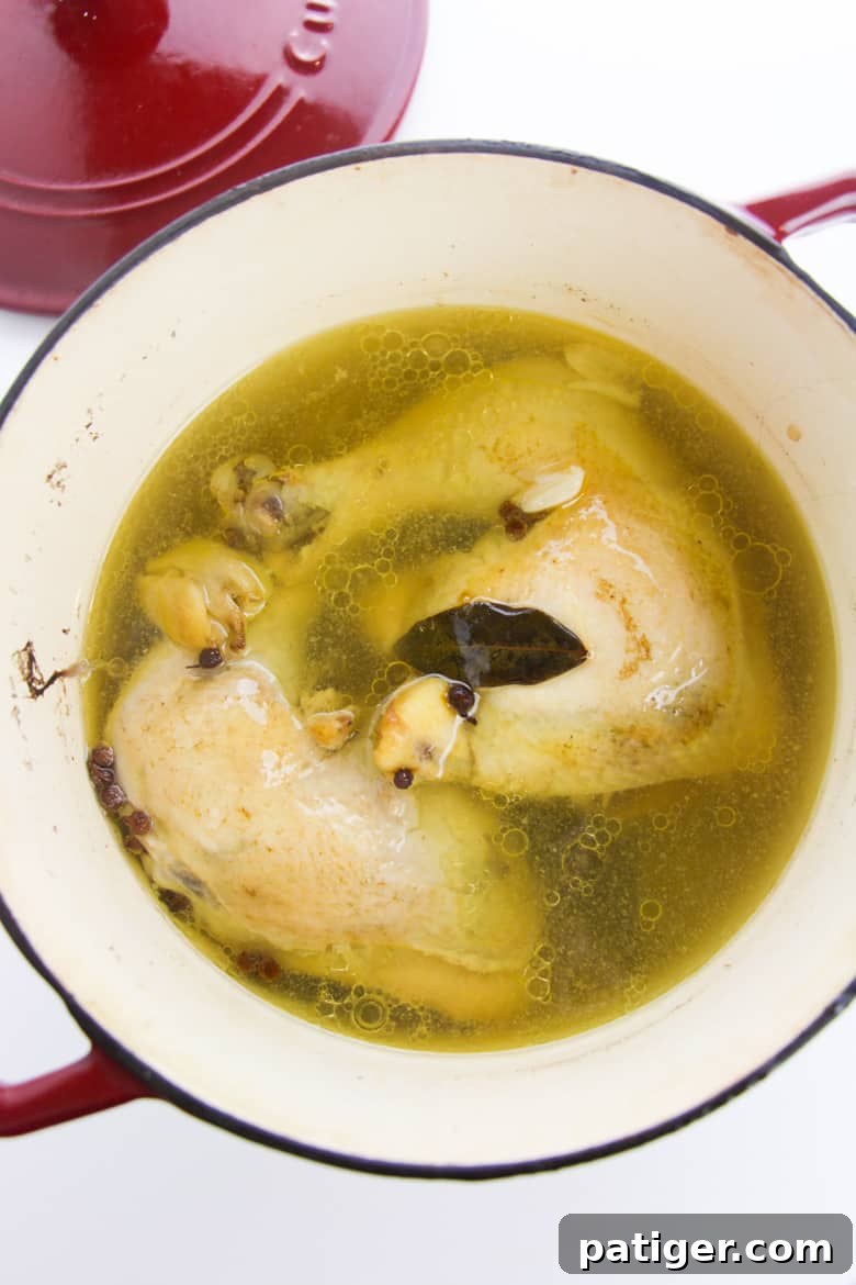 Two succulent poached chicken leg quarters gently simmering in a rich chicken broth infused with herbs and spices in a large pot.