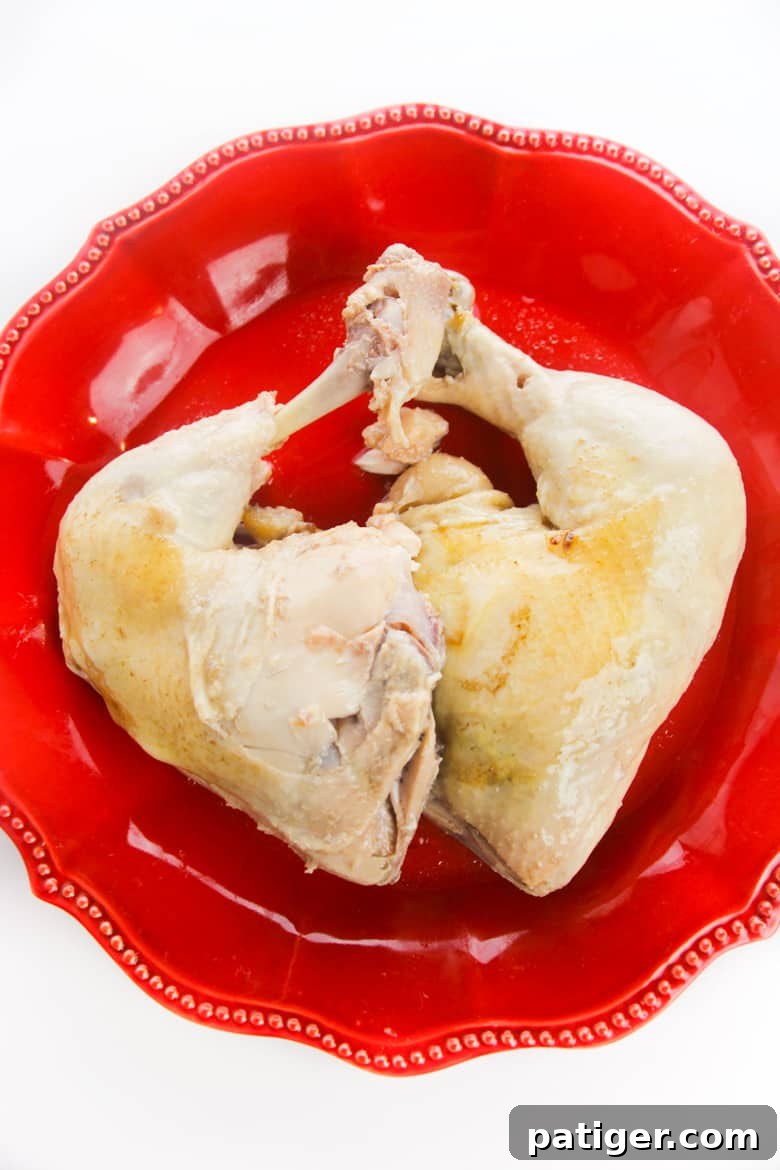 A pair of beautifully cooked chicken quarters, perfectly poached and resting on a red plate, ready for the next step of shredding.