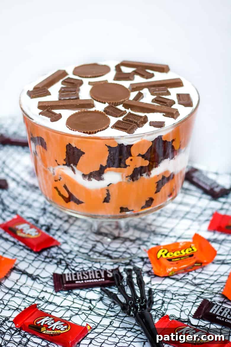 A vibrant Halloween Trifle made with HERSHEY® Halloween Candy, featuring layers of chocolate brownie, orange pudding, and white whipped topping, garnished with REESE’S Peanut Butter Cups, KIT KAT® Bars, and HERSHEY’S Milk Chocolate.