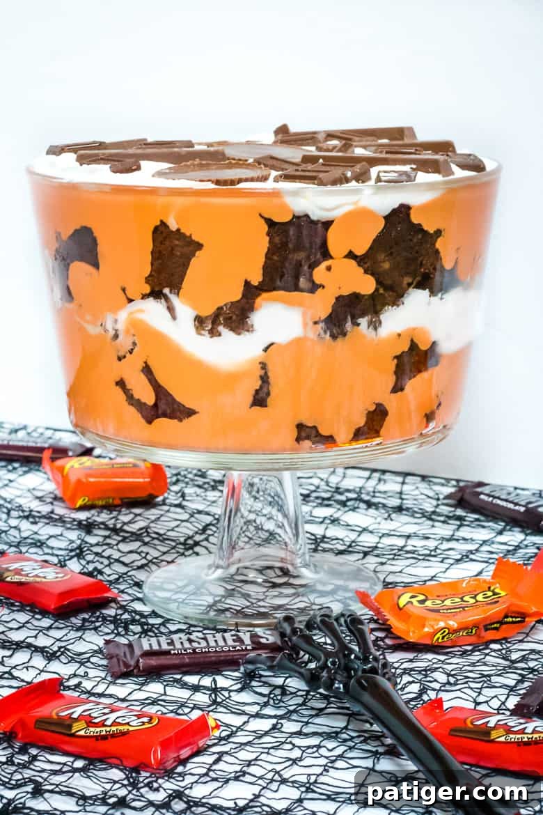 A delightful slice of Halloween Candy Trifle served in a clear glass, highlighting the layers of brownie, orange pudding, and whipped topping, adorned with HERSHEY® Halloween candies.
