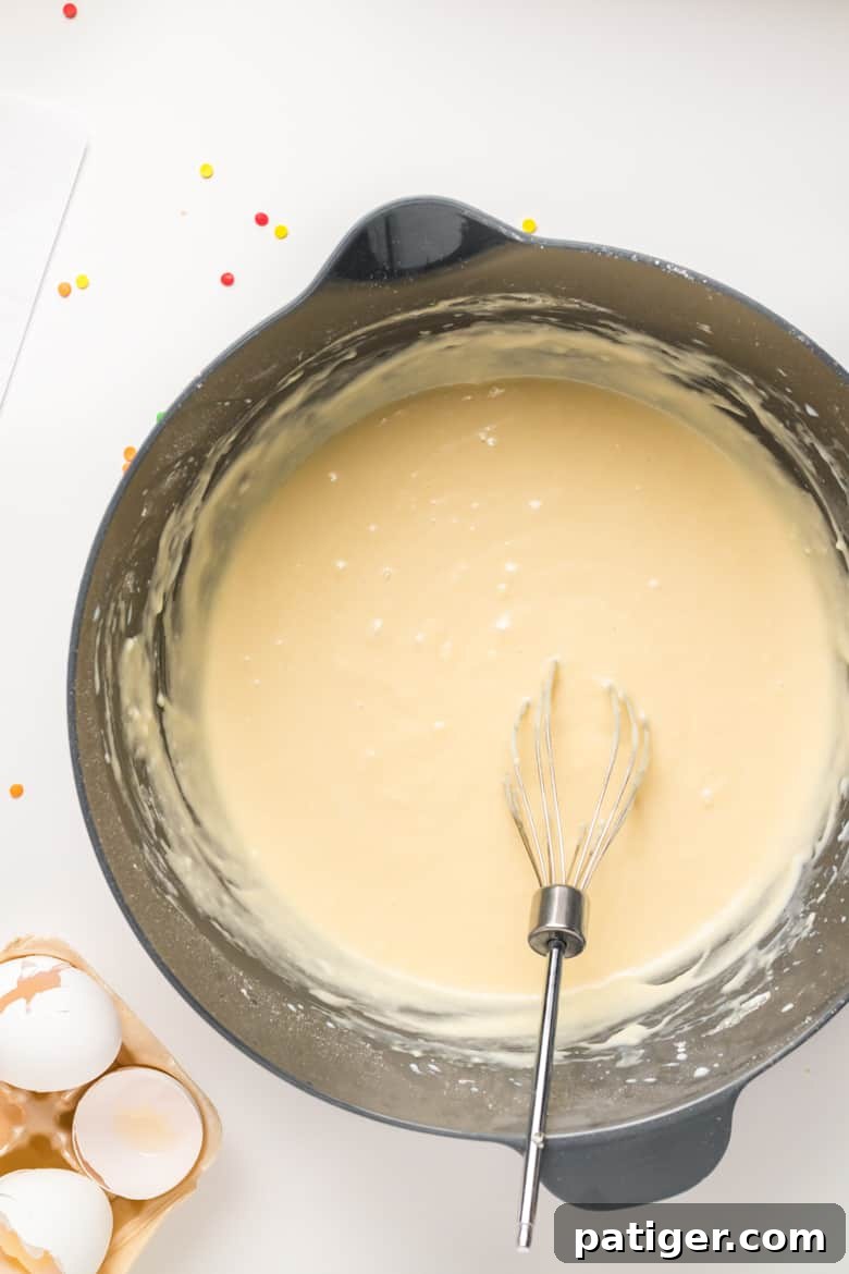 Vanilla cupcake batter in a silver bowl with a wire whisk