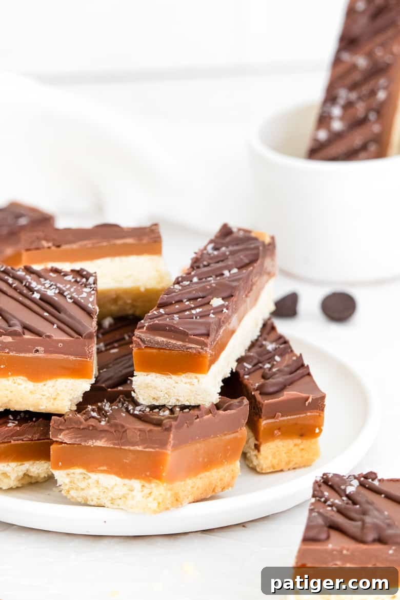 Homemade Twix bars with layers of buttery shortbread, soft caramel, and smooth chocolate, garnished with a sprinkle of sea salt.
