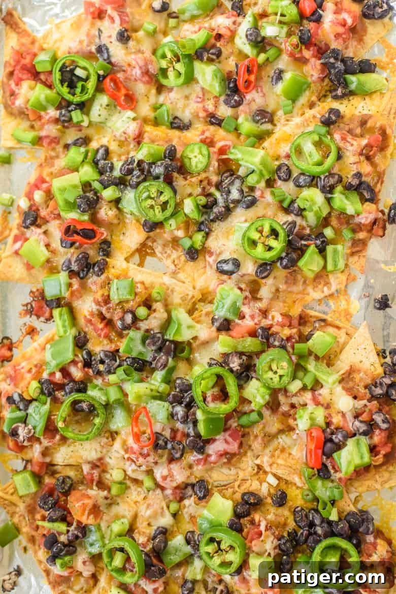 Sheet pan filled with vegetarian nachos featuring refried beans, black beans, salsa, melted cheese, and sliced jalapeños