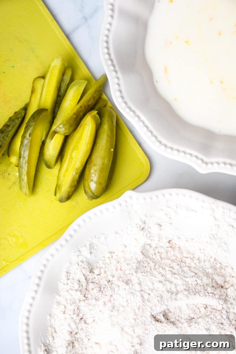 Pickle spears on cutting board, bowl of flour coating, bowl of egg and milk mixture