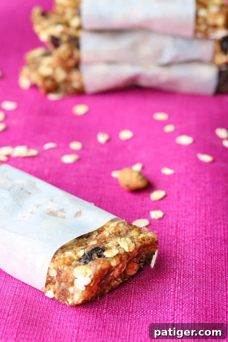 Homemade cherry almond granola bars on a pink tablecloth, with whole rolled oats sprinkled around, suggesting natural ingredients and rustic charm.