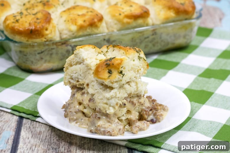 A single serving of biscuits and gravy breakfast casserole on a white plate, with the full 9x13 inch pan visible in the background.
