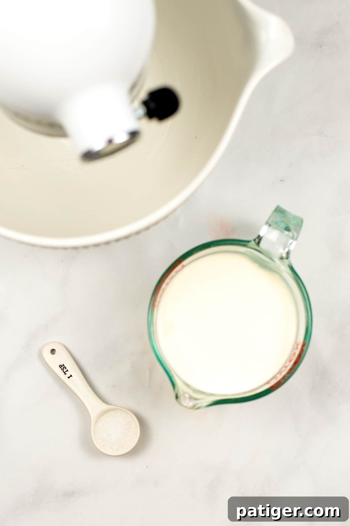 Stand mixer, measuring cup filled with cream, and teaspoon of salt