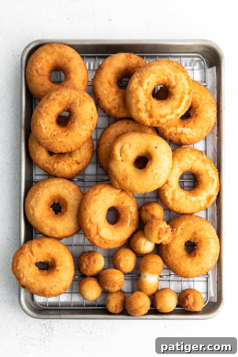 Golden brown freshly fried doughnuts on metal cooling rack over sheet pan