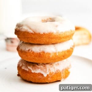 Three glazed doughnuts stacked on top of one another, set atop a white plate