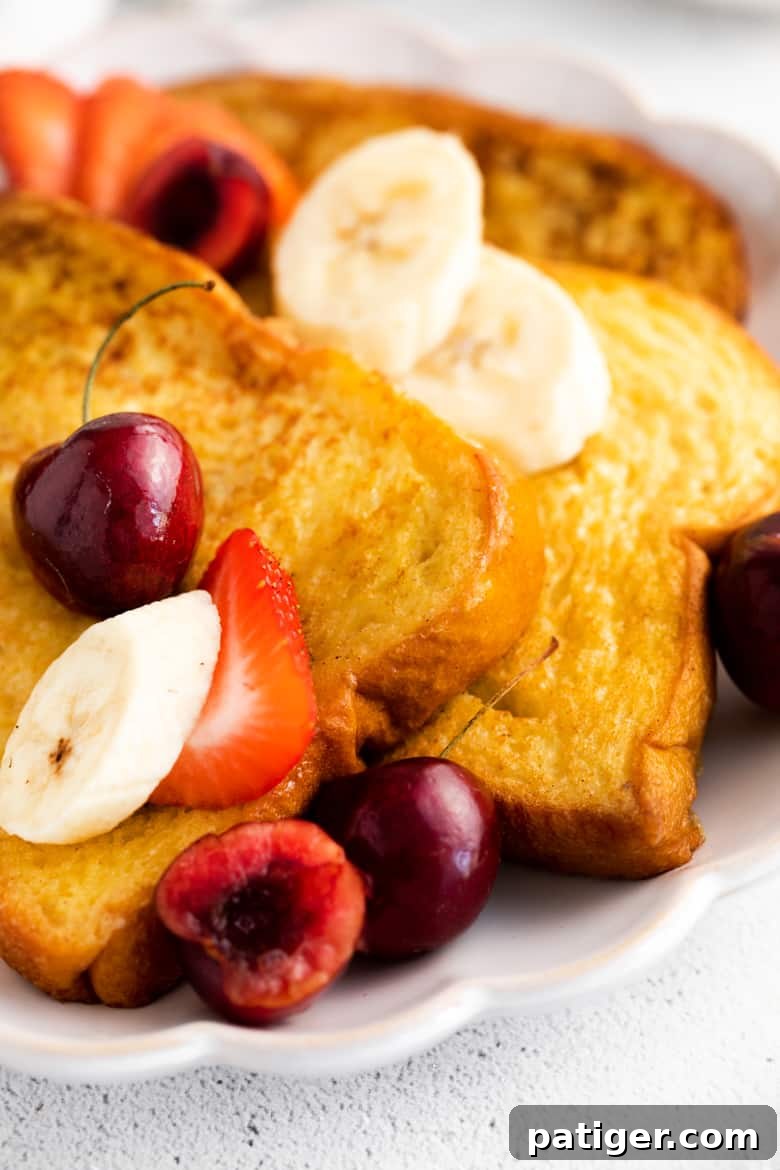 Thick sliced fluffy brioche french toast topped with slices of banana and strawberries, and fresh cherries.
