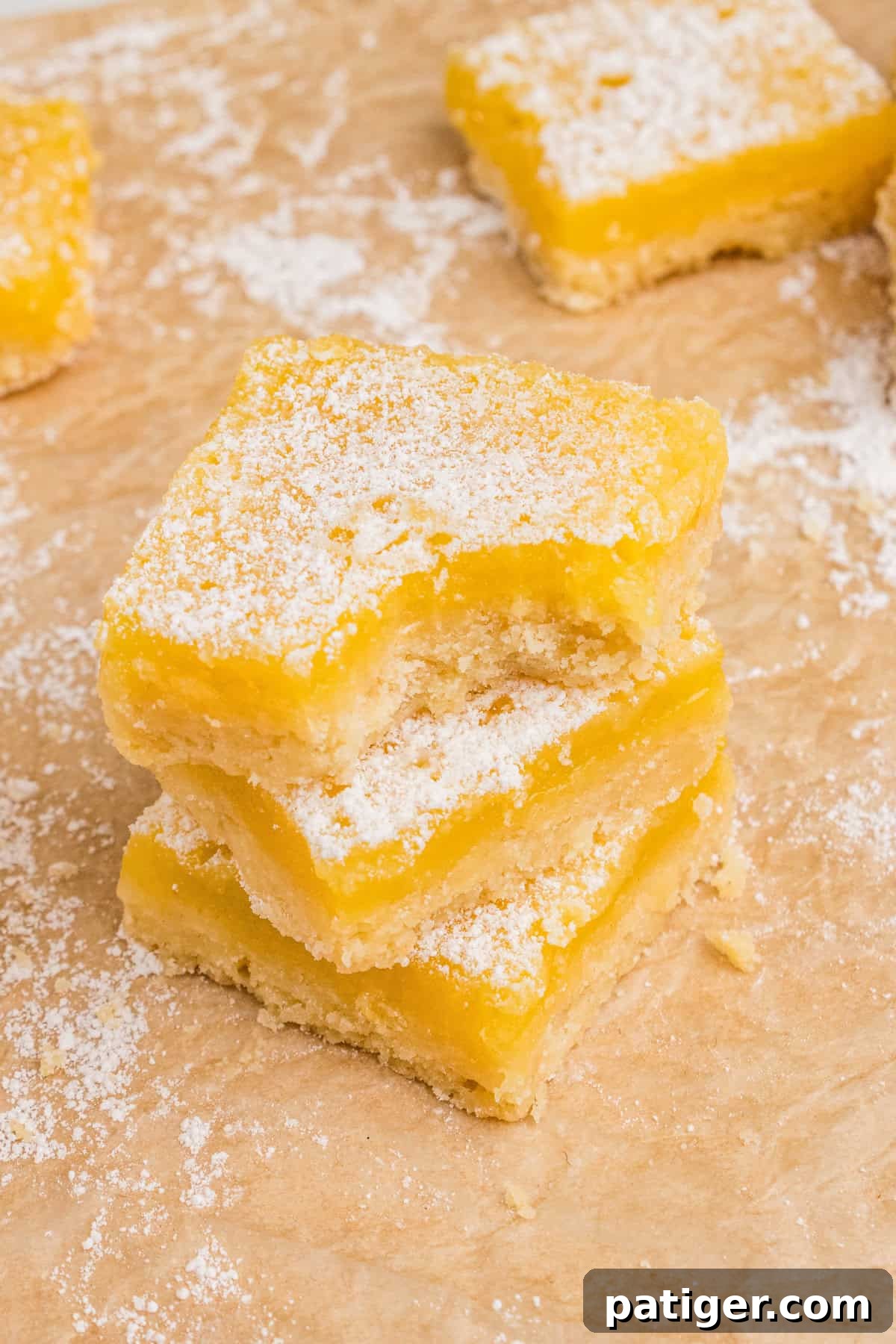 Lemon bars with shortbread crust and dusting of powdered sugar. Three square bars are stacked and the top bar has a bite taken out of it.