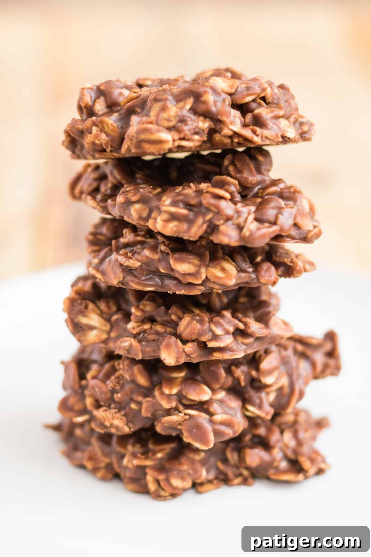 Six thick chocolate peanut butter oatmeal no bake cookies stacked one on top of another on a white plate.