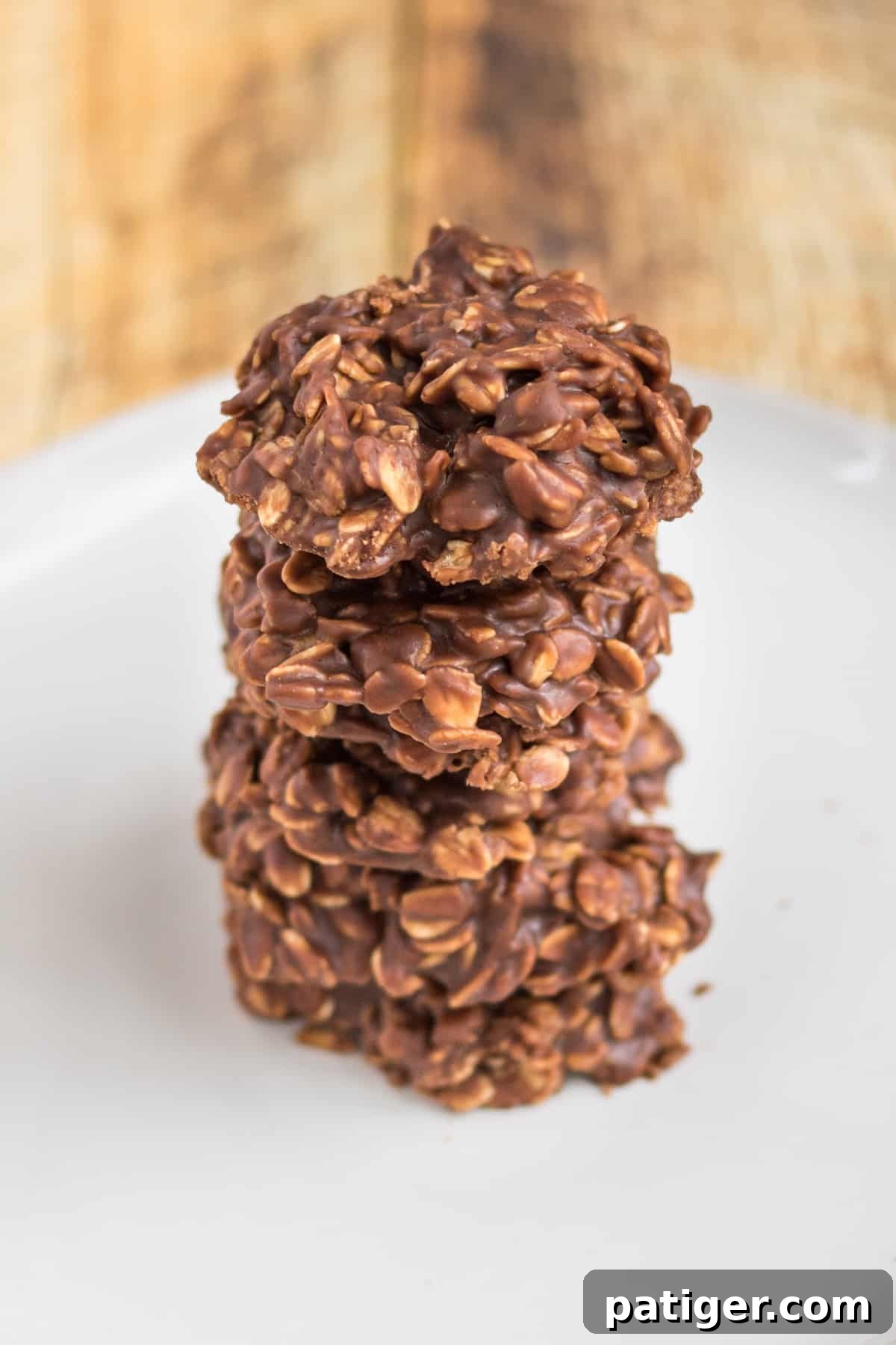Five thick chocolate oatmeal cookies stacked one on top of another on a white plate.
