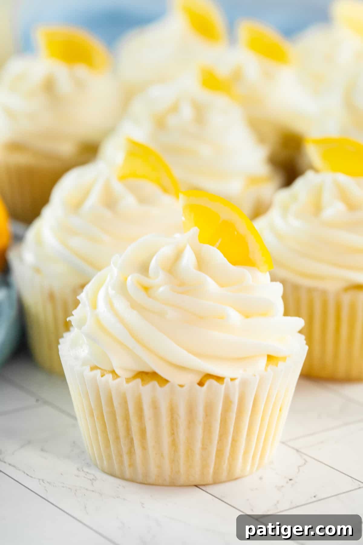 Lemon cupcakes topped with cream cheese frosting and garnished with a slice of lemon, presented elegantly on a serving tray.