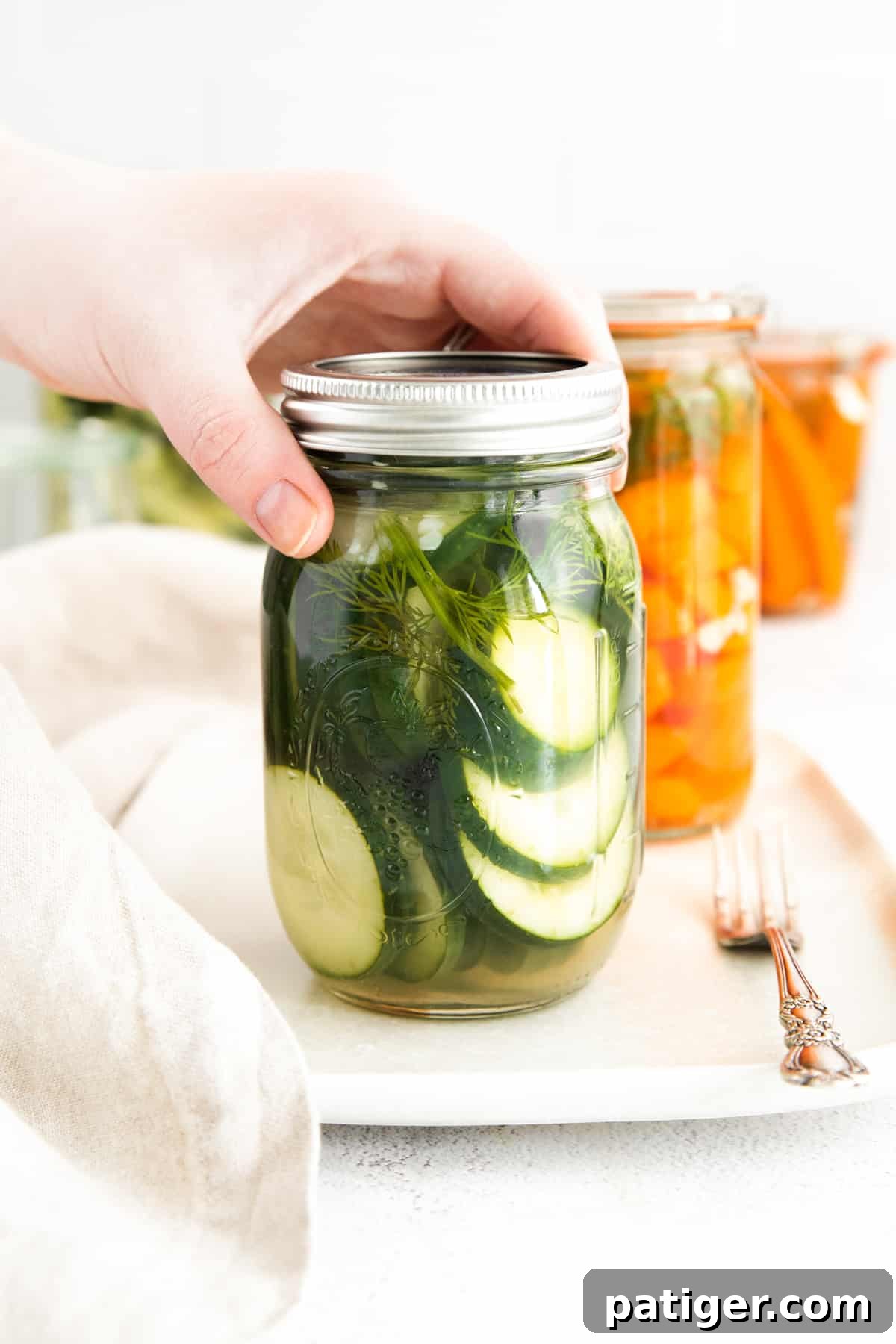 Effortless Fridge Pickles 8 A hand placing a lid on a jar of freshly made refrigerator pickles.