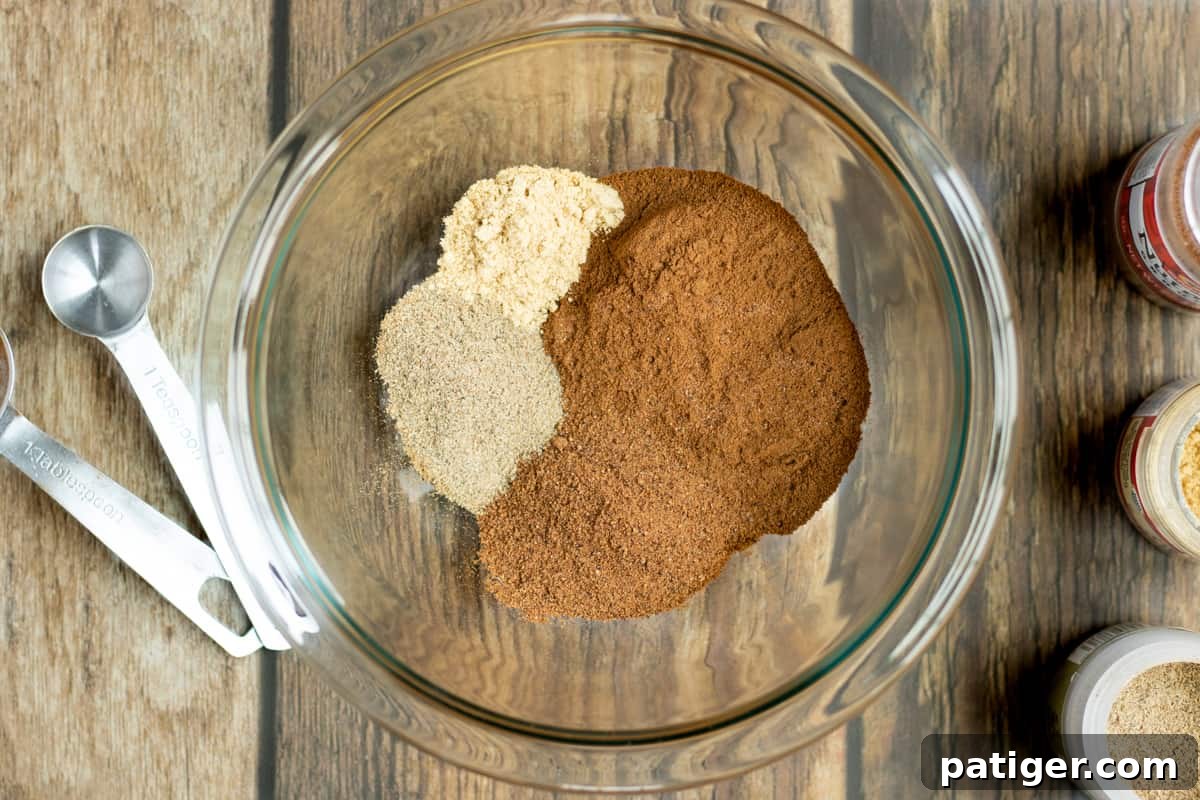 Autumn Orchard Spice 3 glass bowl with cinnamon, nutmeg, cardamon, and ginger. Measuring spoons and spice jars are next to the bowl