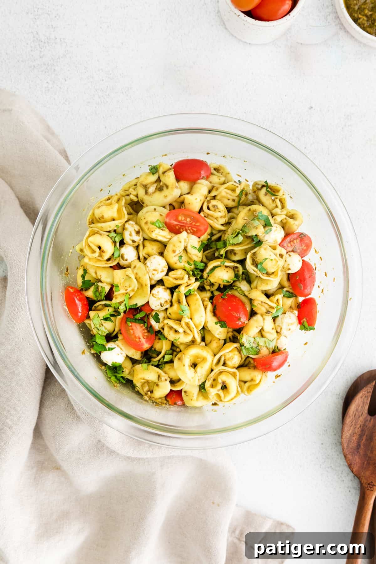 A serving bowl filled with a beautifully tossed pesto tortellini pasta salad, garnished with fresh basil, ready to be enjoyed.