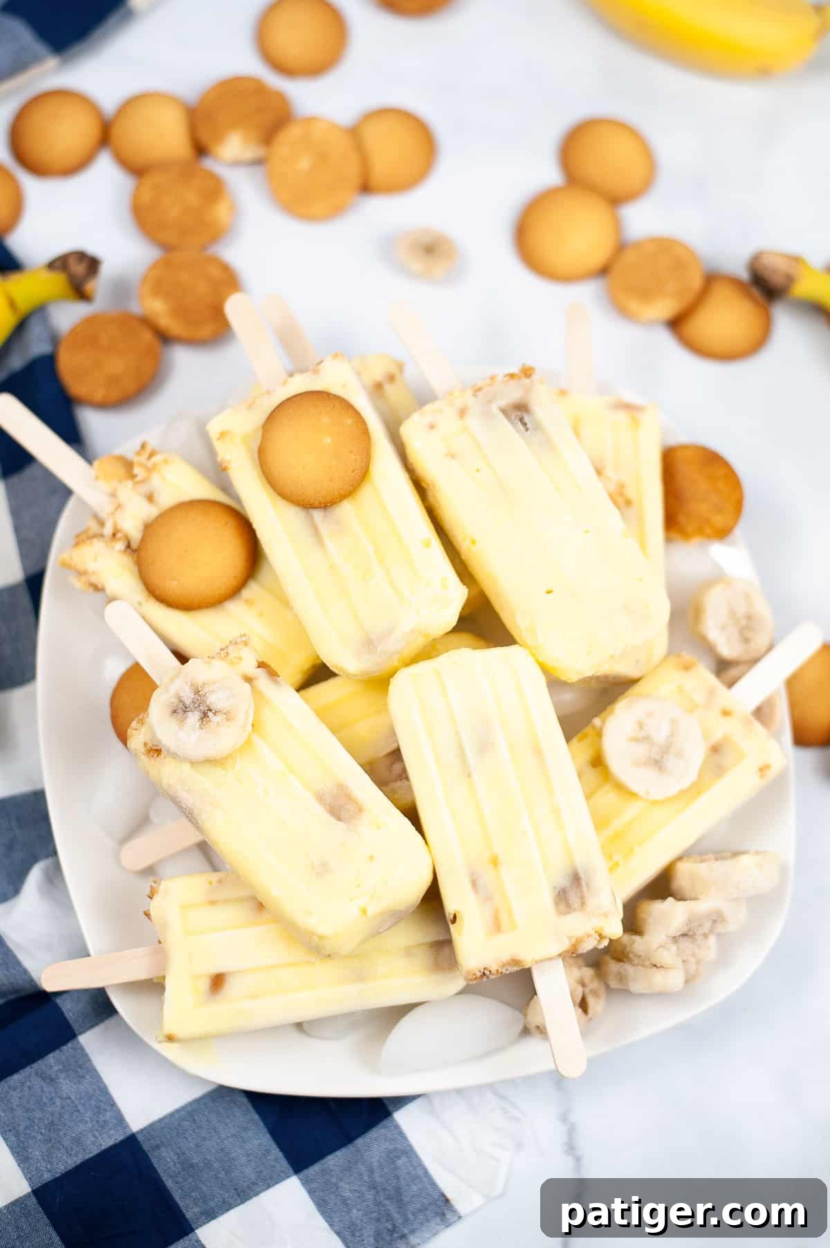 Velvet Banana Pudding Pops 2 Banana popsicles piled on a platter with nilla wafers and frozen banana slices, inviting a taste of summer