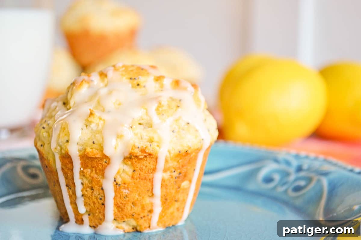 Zesty Lemon Poppy Seed Muffins 2 A perfectly baked lemon poppy seed muffin, generously drizzled with a sweet lemon glaze that drips down its sides, inviting you to take a bite. In the softly blurred background, more delectable muffins and fresh, vibrant lemons hint at the citrusy goodness within.
