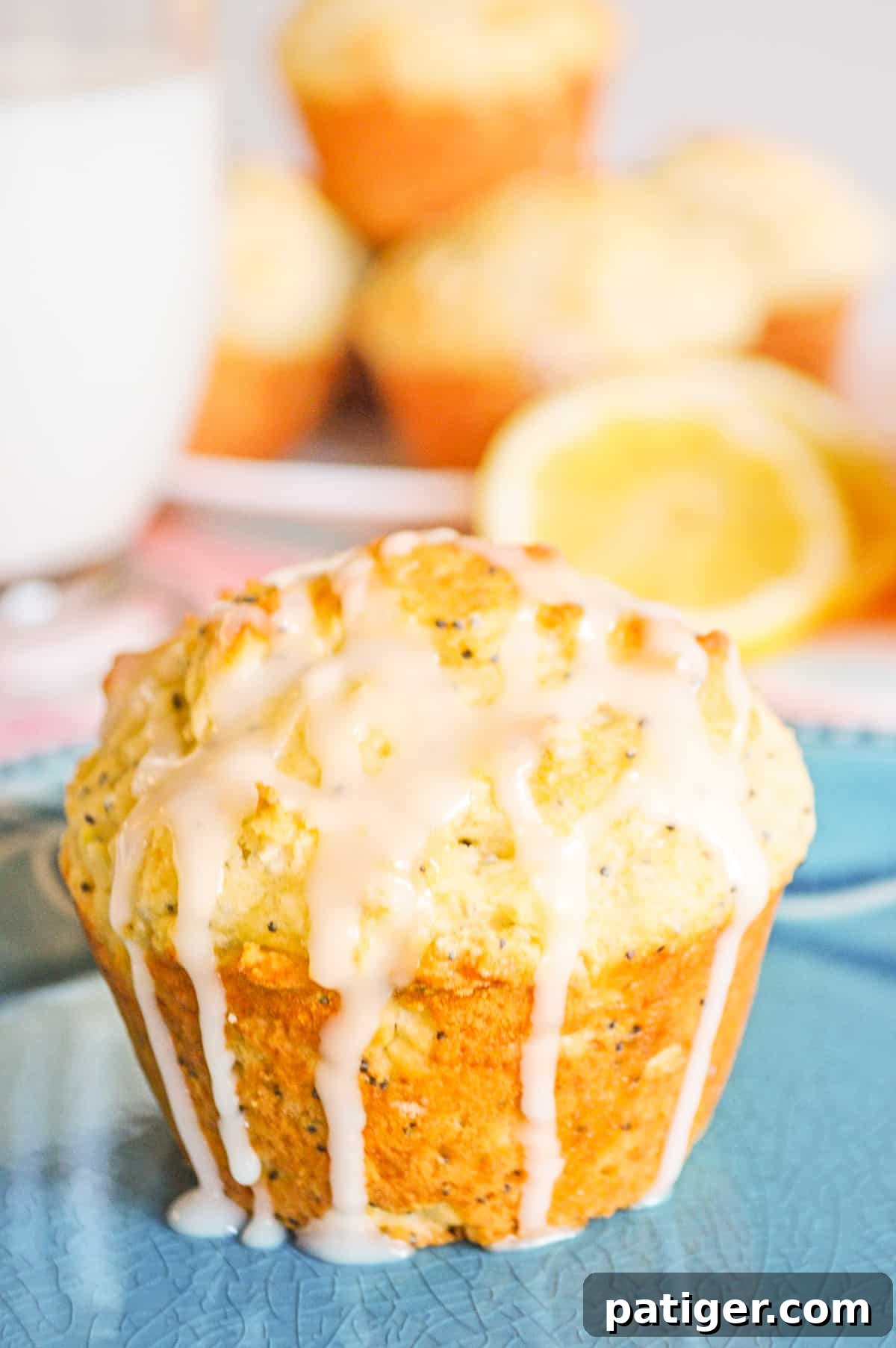 Zesty Lemon Poppy Seed Muffins 5 A close-up of a lemon poppy seed muffin, generously coated in a sweet lemon glaze that is elegantly dripping down its sides. Additional muffins and freshly sliced lemons are artfully arranged in the background, highlighting the zesty essence of the treat.