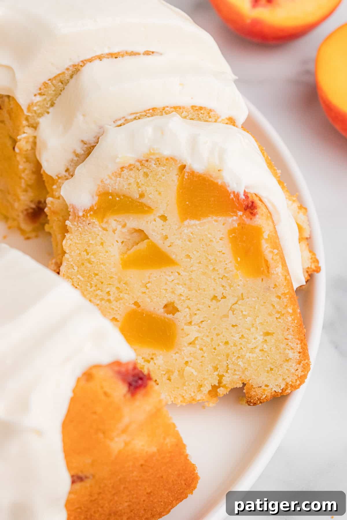 A sliced peach pound cake arranged on a white plate. The peach cake is topped with cream cheese icing, and the interior reveals multiple peach chunks.