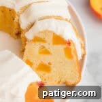 A sliced peach pound cake with cream cheese frosting and multiple chunks of fresh peaches distributed throughout.