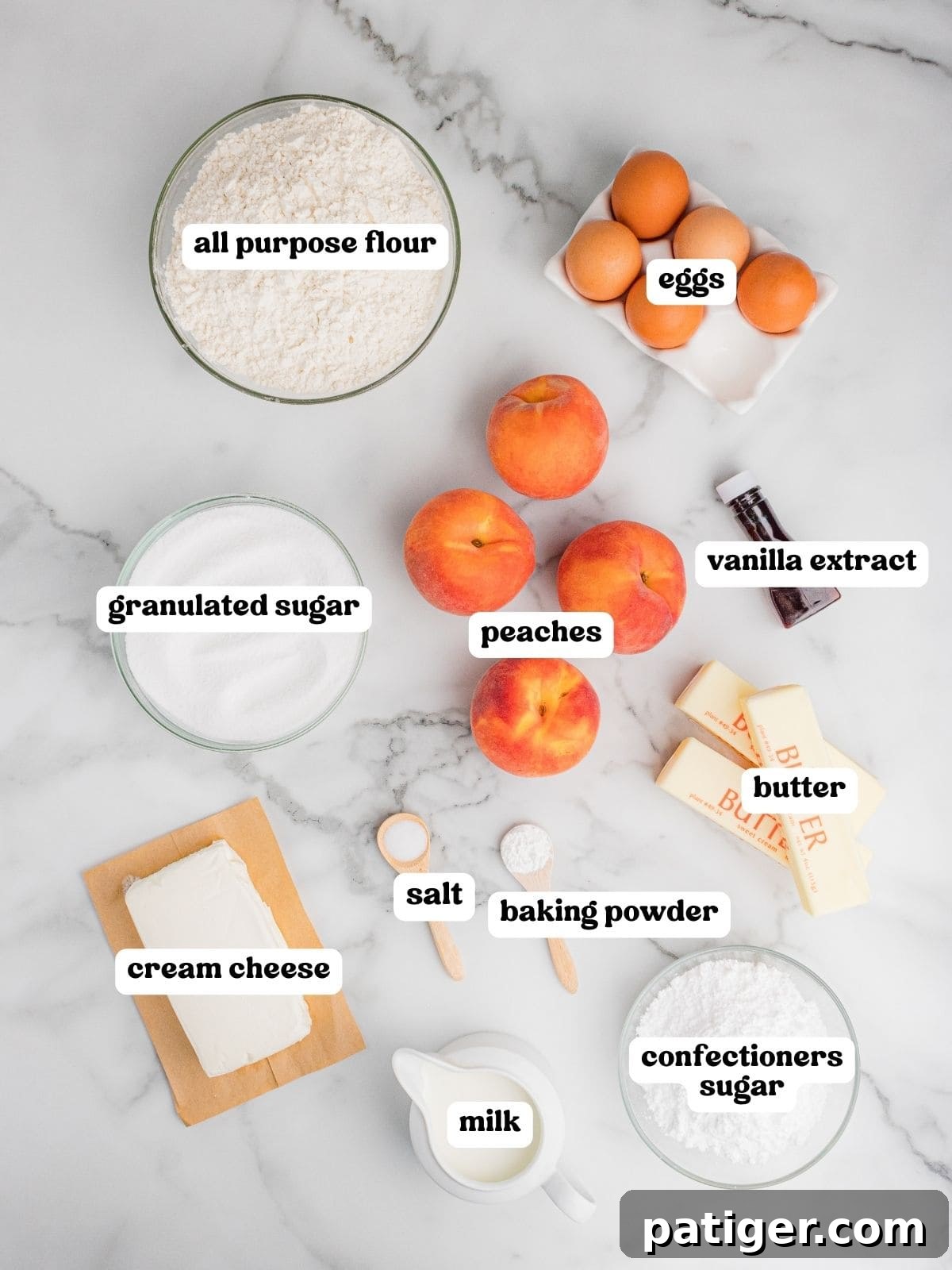 Overhead view of ingredients arranged on a marble surface for peach cake, each labeled: all purpose flour, eggs, granulated sugar, peaches, vanilla extract, butter, cream cheese, salt, baking powder, milk, and confectioners sugar.