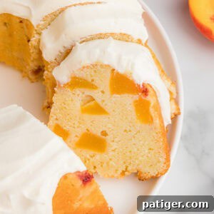 A sliced peach pound cake with cream cheese frosting and multiple chunks of fresh peaches distributed throughout.