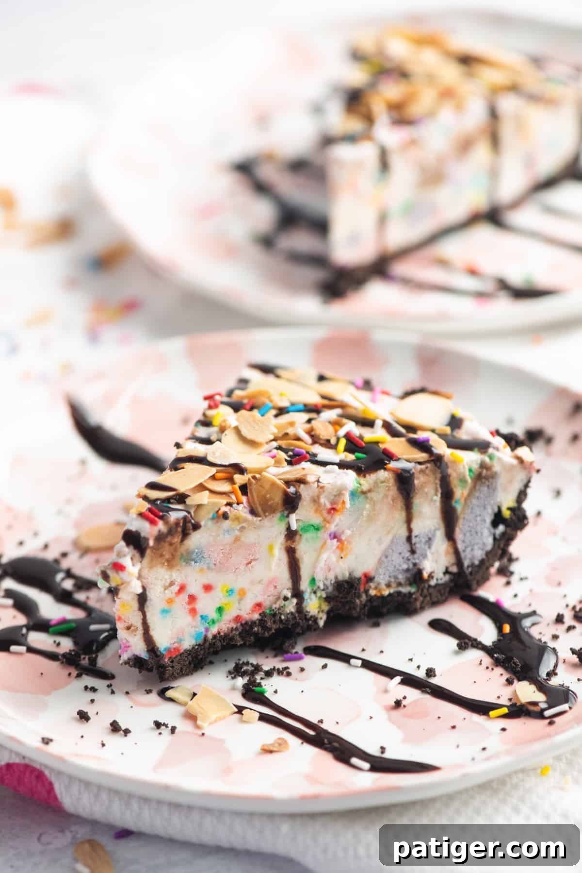 Icebox Indulgence 2 A slice of vanilla ice cream pie with chocolate crust topped with chocolate sauce, rainbow sprinkles, and sliced almonds. Chunks of rainbow cake and sprinkles can be seen inside the vanilla ice cream pie.
