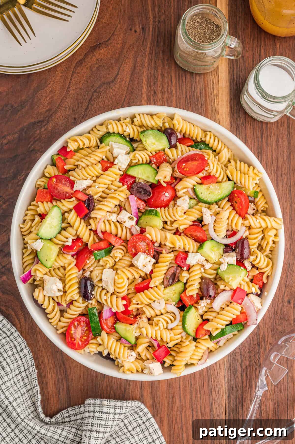A vibrant bowl of Greek pasta salad featuring rotini pasta, halved cherry tomatoes, sliced cucumbers, kalamata olives, crumbled feta cheese, red onion, and red bell pepper, beautifully arranged and ready to serve.