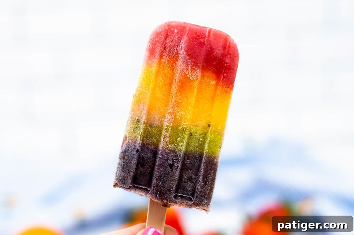 Close-up of a red, orange, yellow, green, and purple fruit ice pop, showing distinct vibrant layers and appetizing texture.