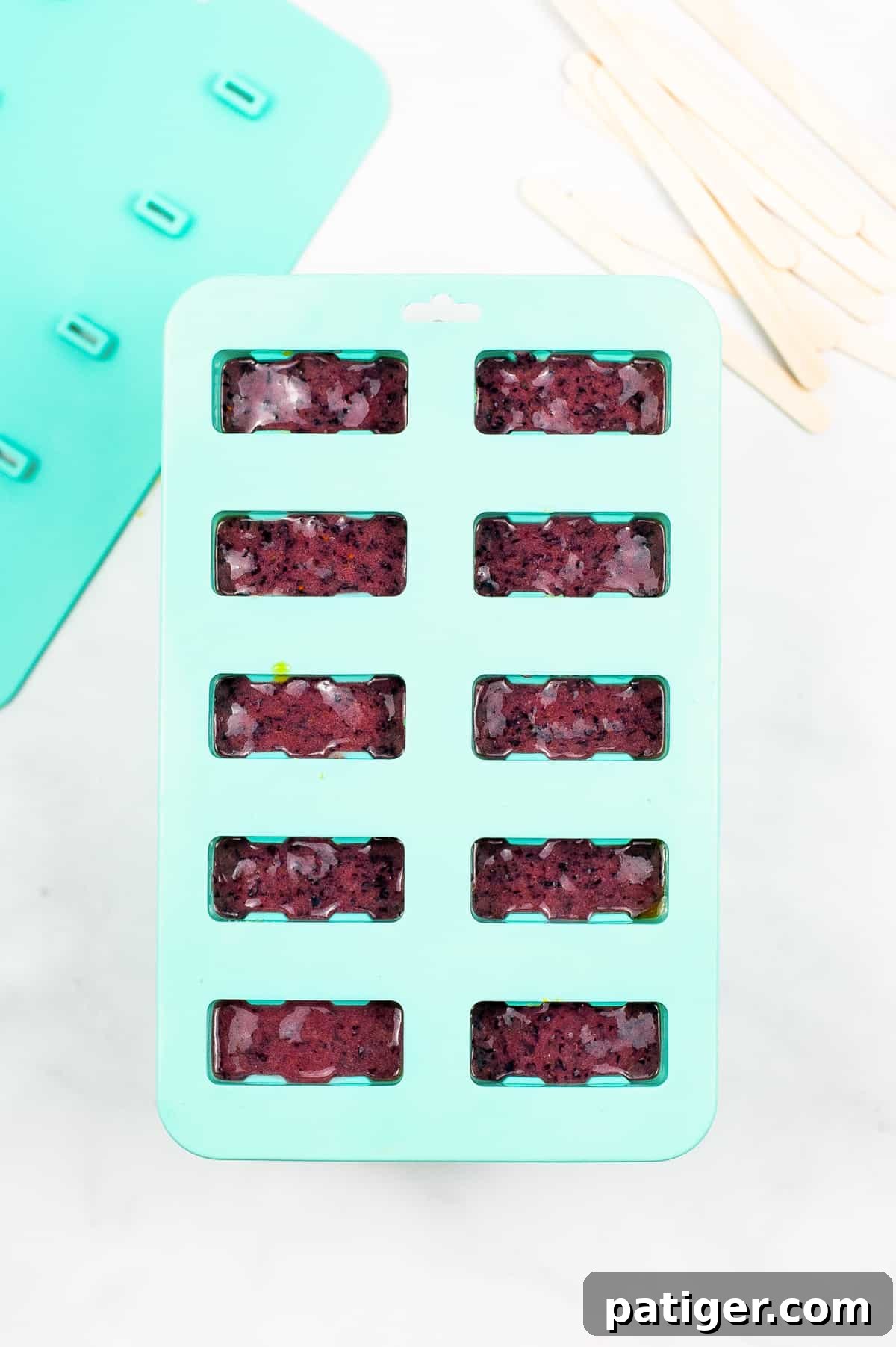 A blue popsicle mold filled with purple ice pops, showing the distinct top layer of the rainbow and the readiness for freezing.