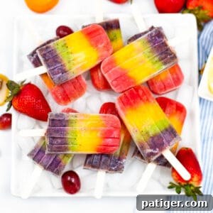 Rainbow popsicles served on a white platter garnished with strawberries and grapes