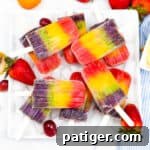 Rainbow popsicles served on a white platter garnished with strawberries and grapes