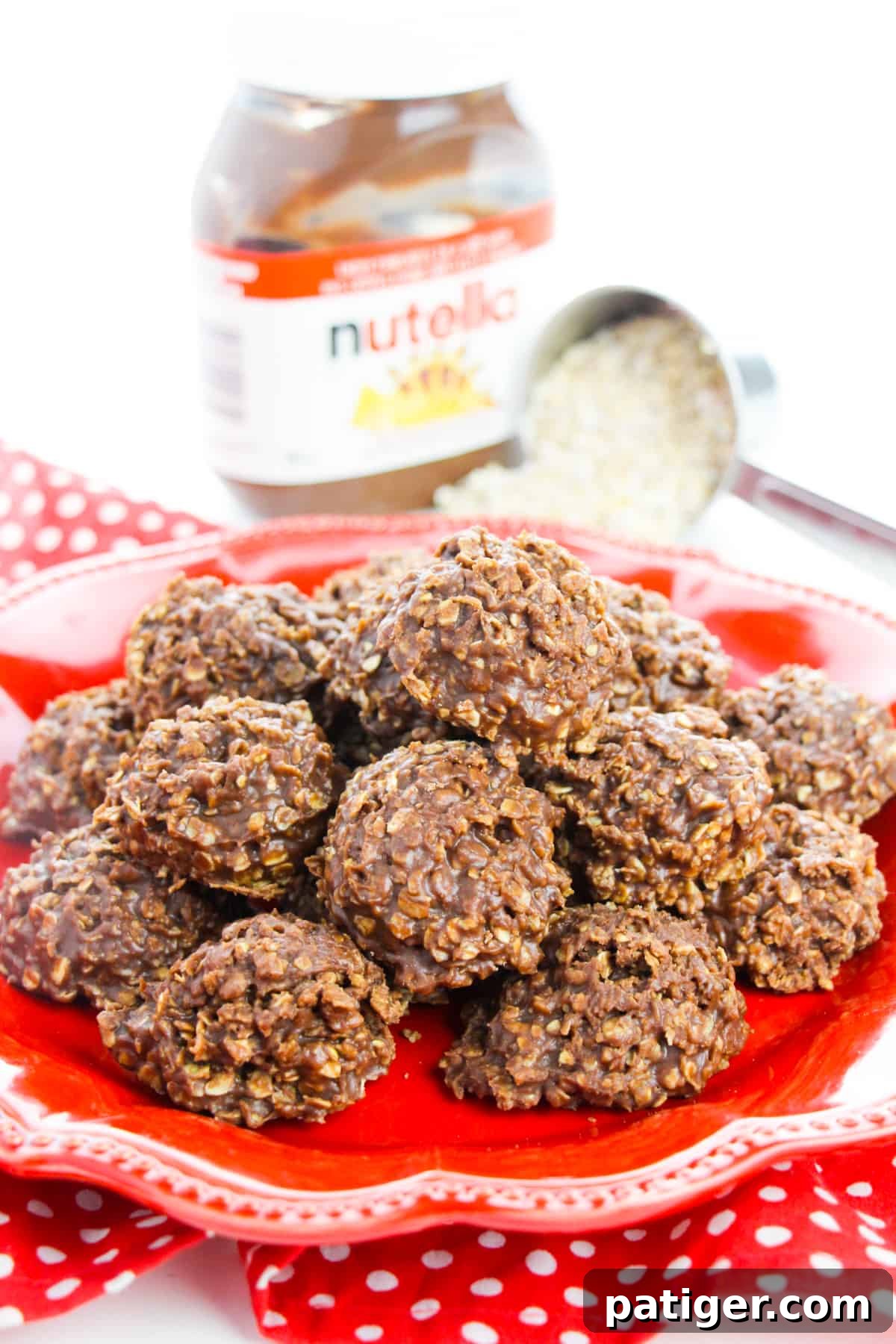 No-bake Nutella Cookies piled on a red plate with scoop of oats and jar of nutella spread behind them