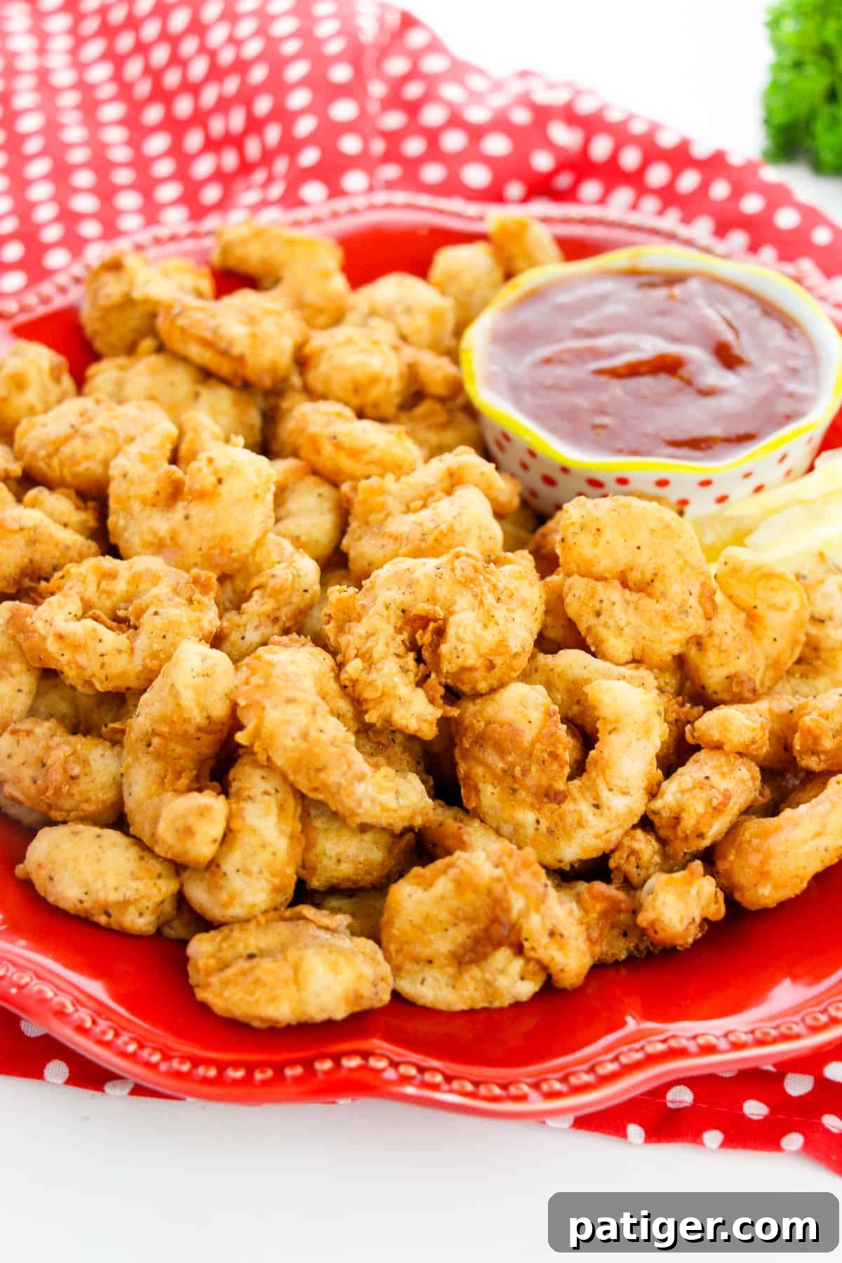 Golden Shrimp Poppers 2 Crispy golden popcorn shrimp served on a vibrant red plate with a side of zesty cocktail sauce, complemented by a rustic red cloth napkin in the background.