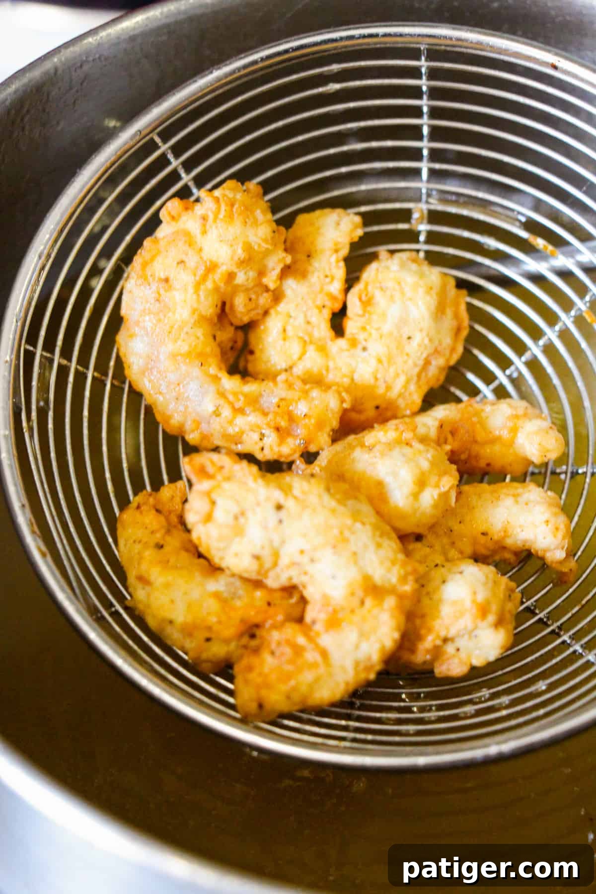 Golden Shrimp Poppers 7 A spider strainer carefully lifts golden-brown fried shrimp from hot oil, demonstrating the perfect moment of readiness.