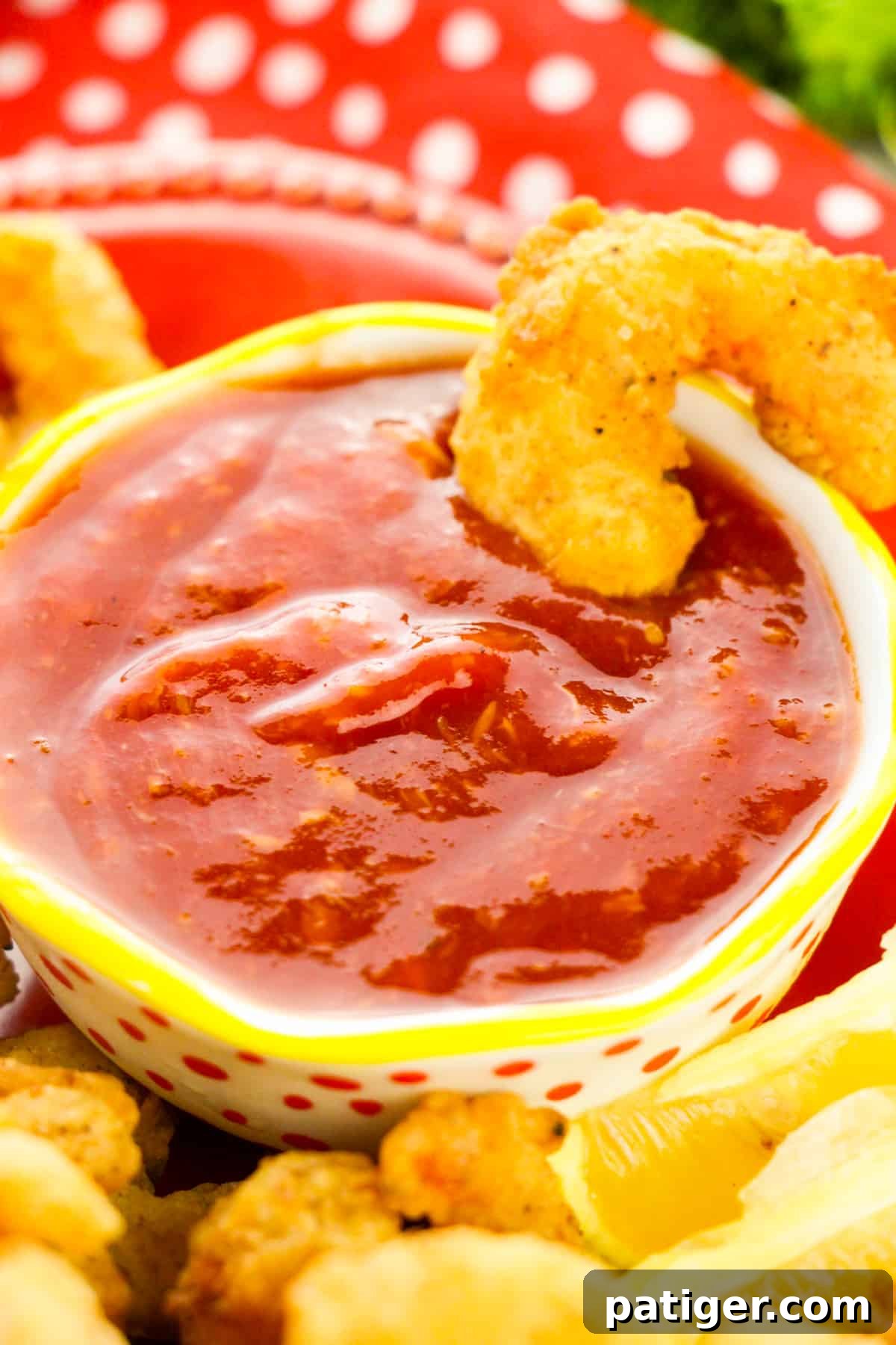 Golden Shrimp Poppers 8 A vibrant red plate showcasing perfectly fried shrimp, with a cup of zesty cocktail sauce strategically placed for dipping, highlighting the delicious pairing.
