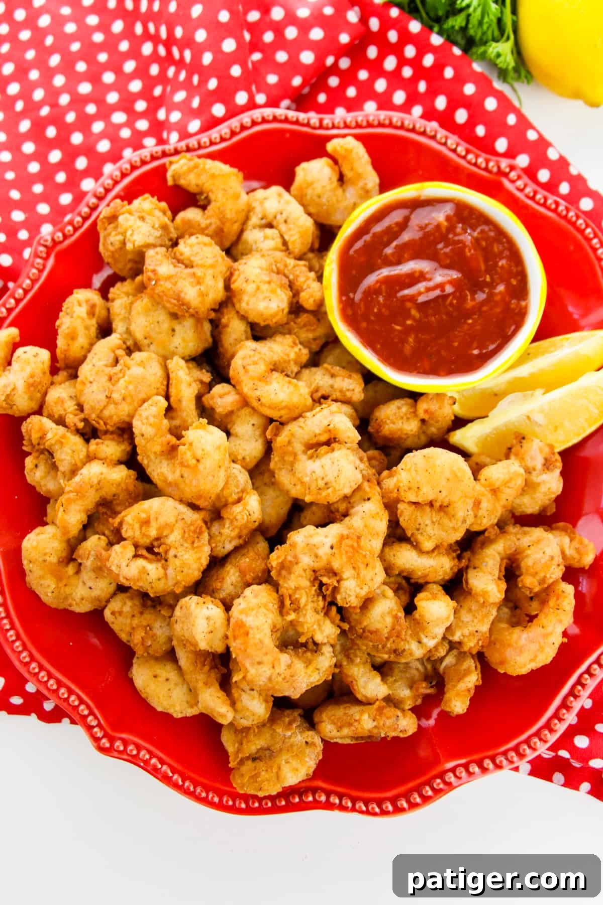 Golden Shrimp Poppers 9 A vibrant red plate featuring a generous serving of popcorn shrimp, artfully garnished with fresh lemon wedges and a side of creamy cocktail sauce for dipping.