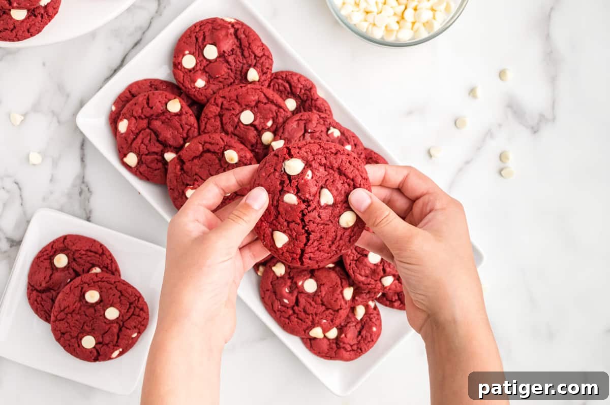 Red velvet cake mix cookies on white platter on countertop. Two hands are reaching into frame and breaking apart one cookie.