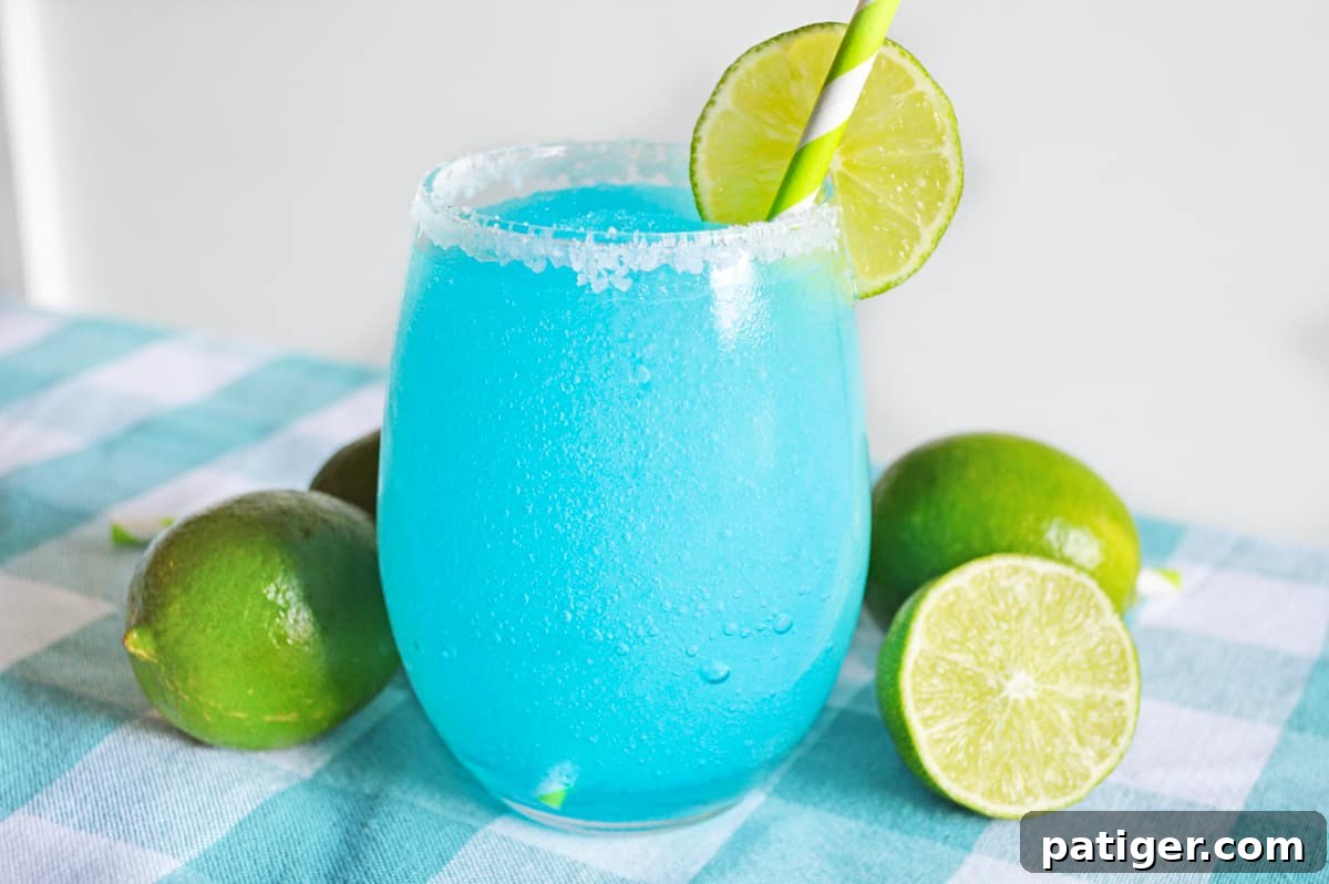 Blue lagoon margarita served in stemless glass rimmed with sugar and garnished with a slice of lime.