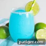 Blue lagoon margarita served in stemless glass rimmed with sugar and garnished with a slice of lime.